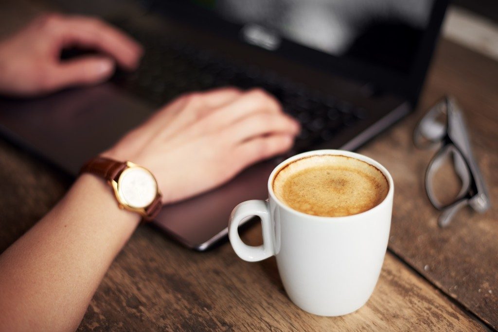 close up photo of hands typing in a laptop with a coffee at the side