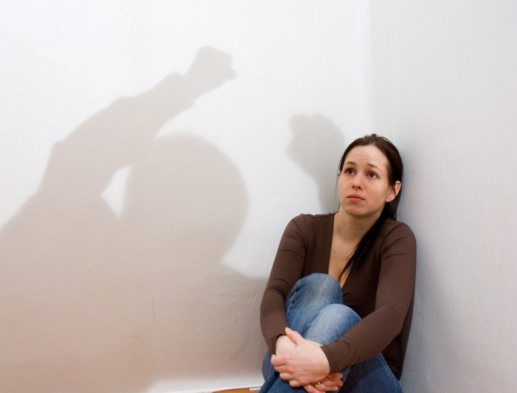 woman cowering in a corner with a shadow depicting a yelling man
